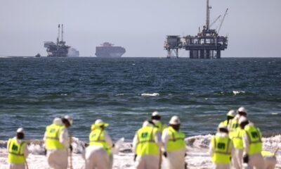 Cleanup workers search for contaminated sand and seaweed in front of drilling platforms and container ships about one week after an oil spill from an offshore oil platform on Oct. 9, 2021, in Huntington Beach, California. (Photo by Mario Tama/Getty Images)