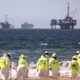 Cleanup workers search for contaminated sand and seaweed in front of drilling platforms and container ships about one week after an oil spill from an offshore oil platform on Oct. 9, 2021, in Huntington Beach, California. (Photo by Mario Tama/Getty Images)