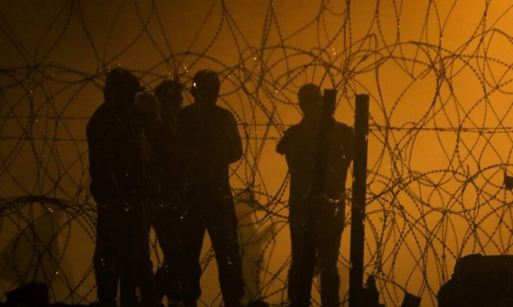 Migrants wait throughout the night on May 10, 2023, in a dust storm at Gate 42, on land between the Rio Grande and the border wall, hoping they will be processed by immigration authorities before the expiration of Title 42. (Photo by Corrie Boudreaux for Source New Mexico)