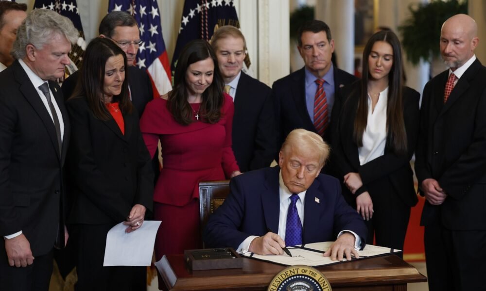 Surrounded by members of Congress and the family of Laken Riley, President Donald Trump signs the Laken Riley Act, the first piece of legislation passed during his second term in office, in the East Room of the White House on Jan. 29, 2025, in Washington, D.C.  U.S. Rep. Mike Collins, a Georgia Republican who represents the district where Riley was killed, is at far left.  (Photo by Chip Somodevilla/Getty Images)