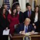 Surrounded by members of Congress and the family of Laken Riley, President Donald Trump signs the Laken Riley Act, the first piece of legislation passed during his second term in office, in the East Room of the White House on Jan. 29, 2025, in Washington, D.C.  U.S. Rep. Mike Collins, a Georgia Republican who represents the district where Riley was killed, is at far left.  (Photo by Chip Somodevilla/Getty Images)