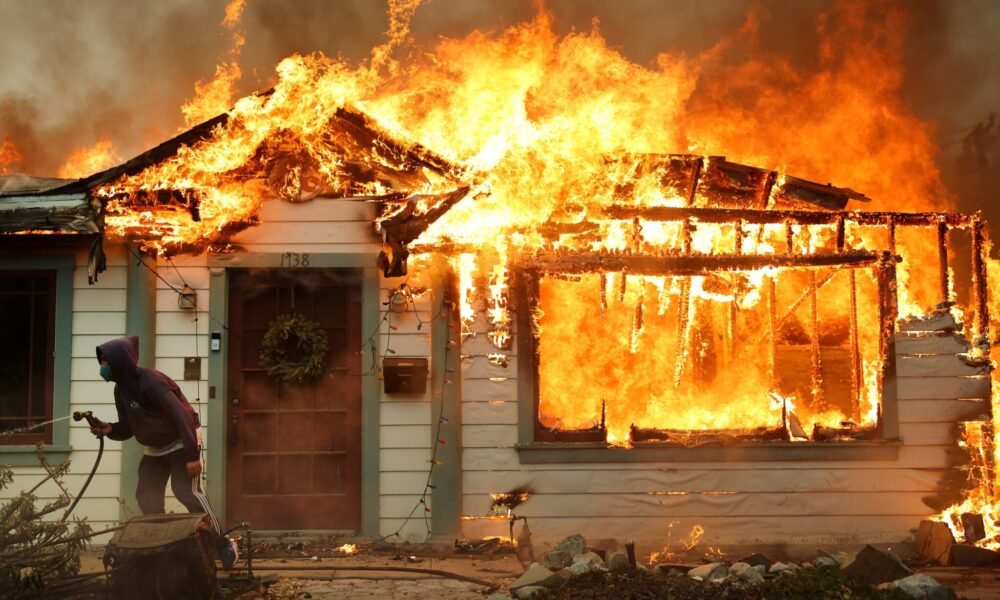 A person uses a garden hose in an effort to save a neighboring home from catching fire during the Eaton Fire on Jan. 8, 2025, in Altadena, California.  (Photo by Mario Tama/Getty Images)